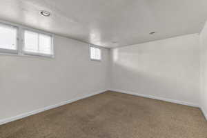 Empty room with a textured ceiling, carpet flooring, and baseboards