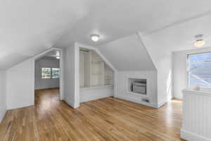 Additional living space featuring built in shelves, a wall unit AC, lofted ceiling, visible vents, and light wood-style flooring