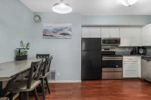 Kitchen featuring visible vents, white cabinetry, appliances with stainless steel finishes, dark stone countertops, and dark wood finished floors