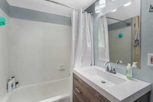 Bathroom with a textured wall, vanity, and shower / bathtub combination with curtain