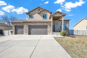 View of front of home with driveway, a garage, stone siding, fence, and stucco siding