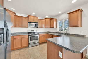 Kitchen featuring light tile patterned floors, dark countertops, a peninsula, stainless steel appliances, and a sink