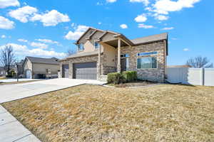 View of front of house featuring a garage, fence, driveway, stone siding, and a front lawn