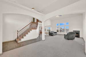 Living room featuring a warm lit fireplace, carpet flooring, stairs, and tile patterned floors