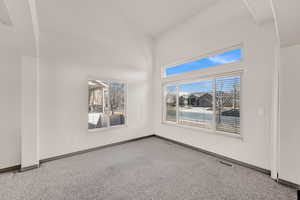 Carpeted spare room featuring a towering ceiling, visible vents, and baseboards