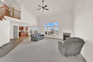 Living area with light tile patterned floors, a tile fireplace, light carpet, ceiling fan with notable chandelier, and baseboards