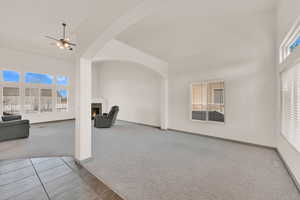 Carpeted living area with baseboards, visible vents, a ceiling fan, a towering ceiling, and a lit fireplace