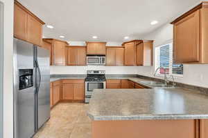 Kitchen with light tile patterned floors, a peninsula, stainless steel appliances, a sink, and recessed lighting