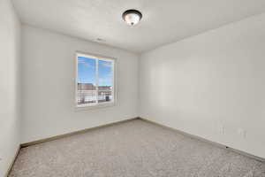 Spare room with a textured ceiling, carpet, visible vents, and baseboards