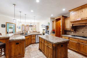 Kitchen with gas cooktop, a sink, a large island, dishwasher, and stone tile flooring