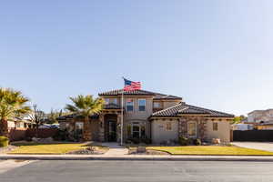 Mediterranean / spanish house featuring stone siding, a tiled roof, fence, a front lawn, and stucco siding