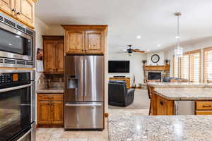 Kitchen featuring a fireplace, stone tile floors, stainless steel appliances, a ceiling fan, and a textured ceiling