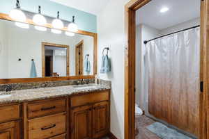 Bathroom with double vanity, a shower with shower curtain, a sink, and toilet