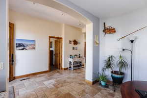 Hallway with baseboards, visible vents, arched walkways, stone tile flooring, and recessed lighting