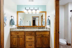 Bathroom with toilet, double vanity, visible vents, and a sink