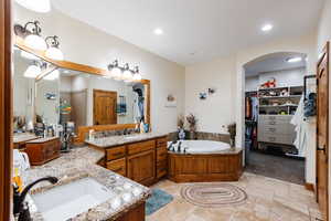 Full bath featuring stone tile floors, a spacious closet, vanity, a bath, and recessed lighting