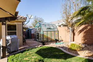 View of yard with a greenhouse, a fenced backyard, and an outbuilding