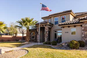 Mediterranean / spanish home featuring stone siding, a tile roof, fence, a front lawn, and stucco siding