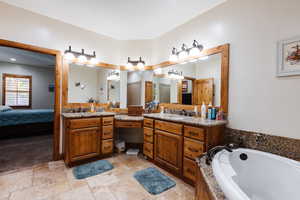 Ensuite bathroom with stone tile flooring, a garden tub, vanity, and connected bathroom