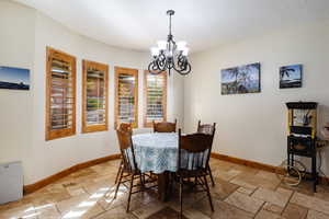 Dining space featuring a chandelier, a textured ceiling, stone tile flooring, and baseboards