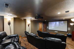 Home theater featuring a textured ceiling, recessed lighting, wood finished floors, visible vents, and baseboards