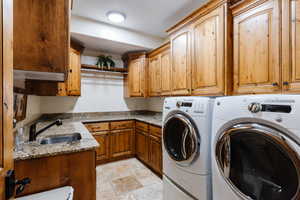 Clothes washing area with cabinet space, washing machine and dryer, stone tile floors, and a sink