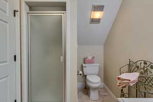 Bathroom featuring toilet, visible vents, baseboards, vaulted ceiling, and a stall shower