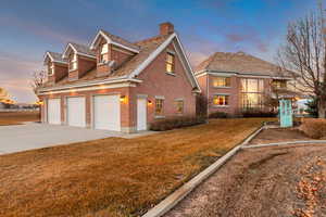 View of front of property featuring brick siding, a yard, a chimney, a garage, and driveway