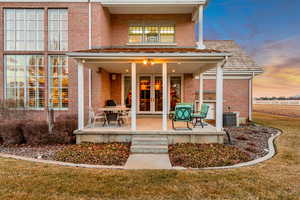 Back of house at dusk with central AC unit, brick siding, french doors, a lawn, and a patio area