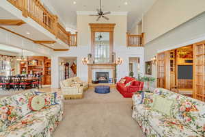 Living area with a towering ceiling, stairway, carpet, a glass covered fireplace, and crown molding