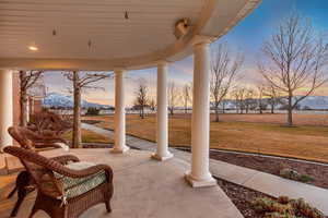 Patio terrace at dusk with covered porch, a lawn, and a mountain view