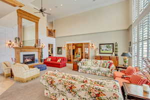 Living room with carpet floors, a decorative wall, a towering ceiling, a ceiling fan, and a glass covered fireplace