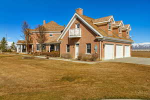 View of front of property with a balcony, brick siding, concrete driveway, a chimney, and a front yard