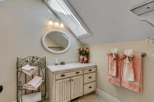 Bathroom with lofted ceiling with skylight, tile patterned flooring, vanity, and baseboards