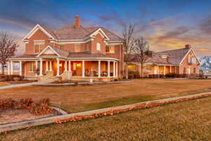 View of front of house with covered porch, brick siding, a yard, and a chimney