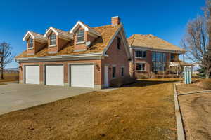 View of front of home with driveway, a garage, a chimney, a front lawn, and brick siding