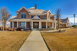 View of front of property featuring a porch, brick siding, a chimney, and a front lawn