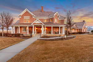 View of front of home with covered porch, brick siding, a chimney, and a front yard