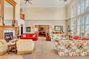 Living area with carpet floors, a glass covered fireplace, a ceiling fan, and crown molding