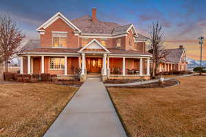 View of front of property featuring a yard, brick siding, a chimney, and a porch