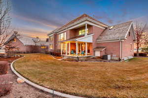 Back of property at dusk featuring a yard, central AC, and brick siding