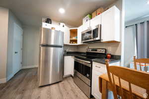 Kitchen featuring open shelves, dark countertops, appliances with stainless steel finishes, light wood-style floors, and white cabinets