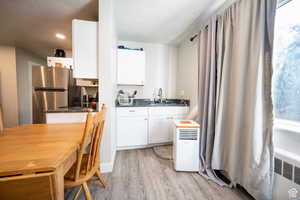 Kitchen featuring dark countertops, freestanding refrigerator, light wood-style floors, white cabinetry, and a sink