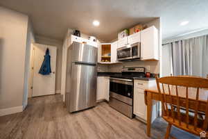 Kitchen with white cabinets, dark countertops, appliances with stainless steel finishes, a textured ceiling, and light wood-type flooring