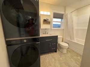 Full bath with shower / bath combination with curtain, toilet, decorative backsplash, stacked washer / dryer, and vanity