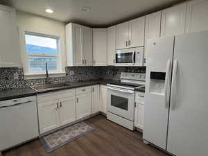 Kitchen with white appliances, dark wood-type flooring, a sink, decorative backsplash, and dark countertops