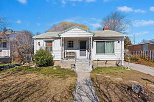 Bungalow-style house featuring covered porch, a front lawn, a chimney, and fence