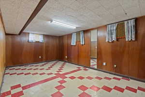 Basement with baseboards, wooden walls, and light floors