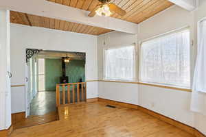 Unfurnished room featuring a wainscoted wall, visible vents, hardwood / wood-style floors, beamed ceiling, and a wood stove