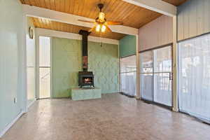 Unfurnished living room featuring a wood stove, a healthy amount of sunlight, beamed ceiling, and wooden ceiling